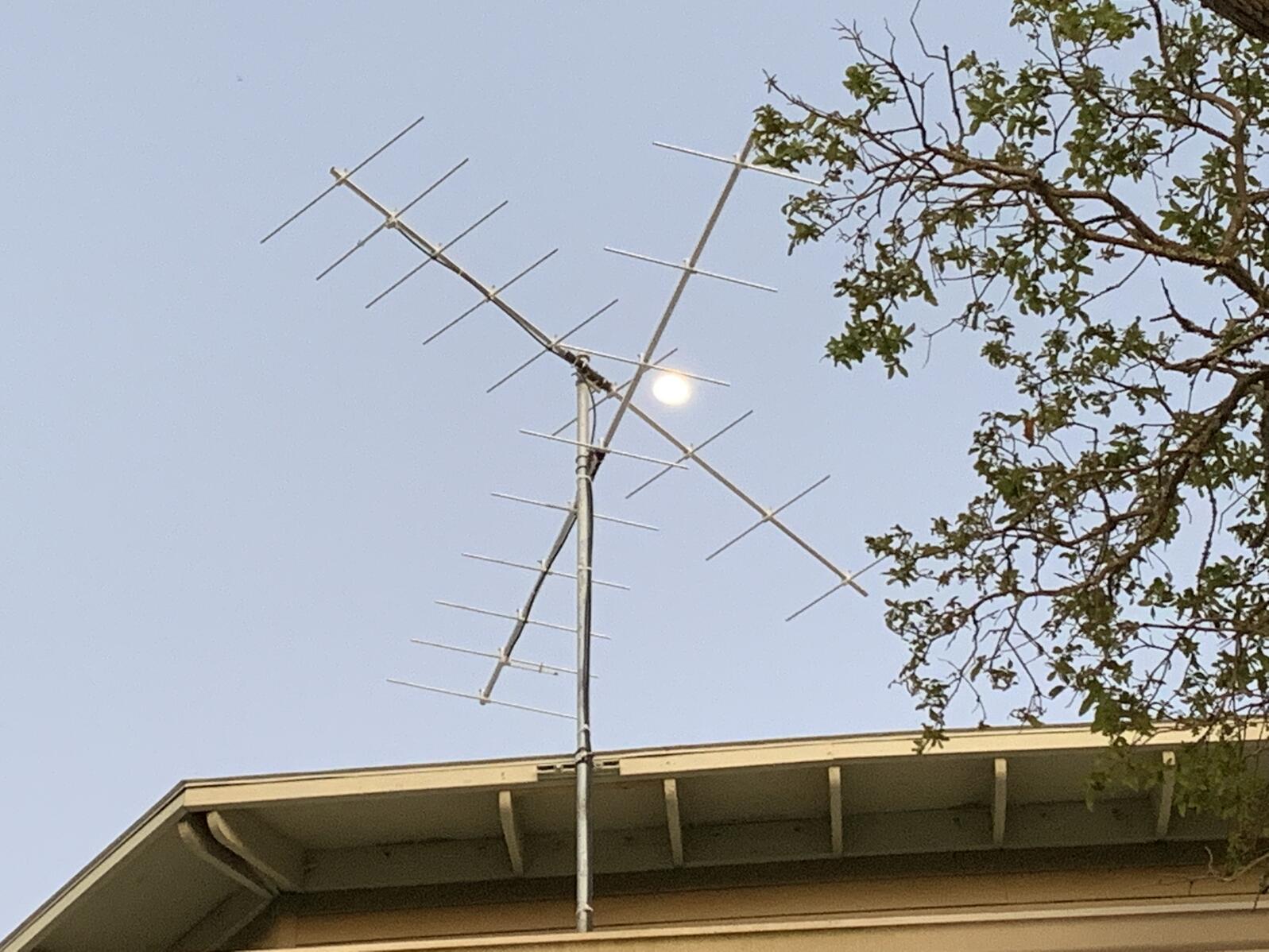 Two antennas on a roof with the moon behind it 