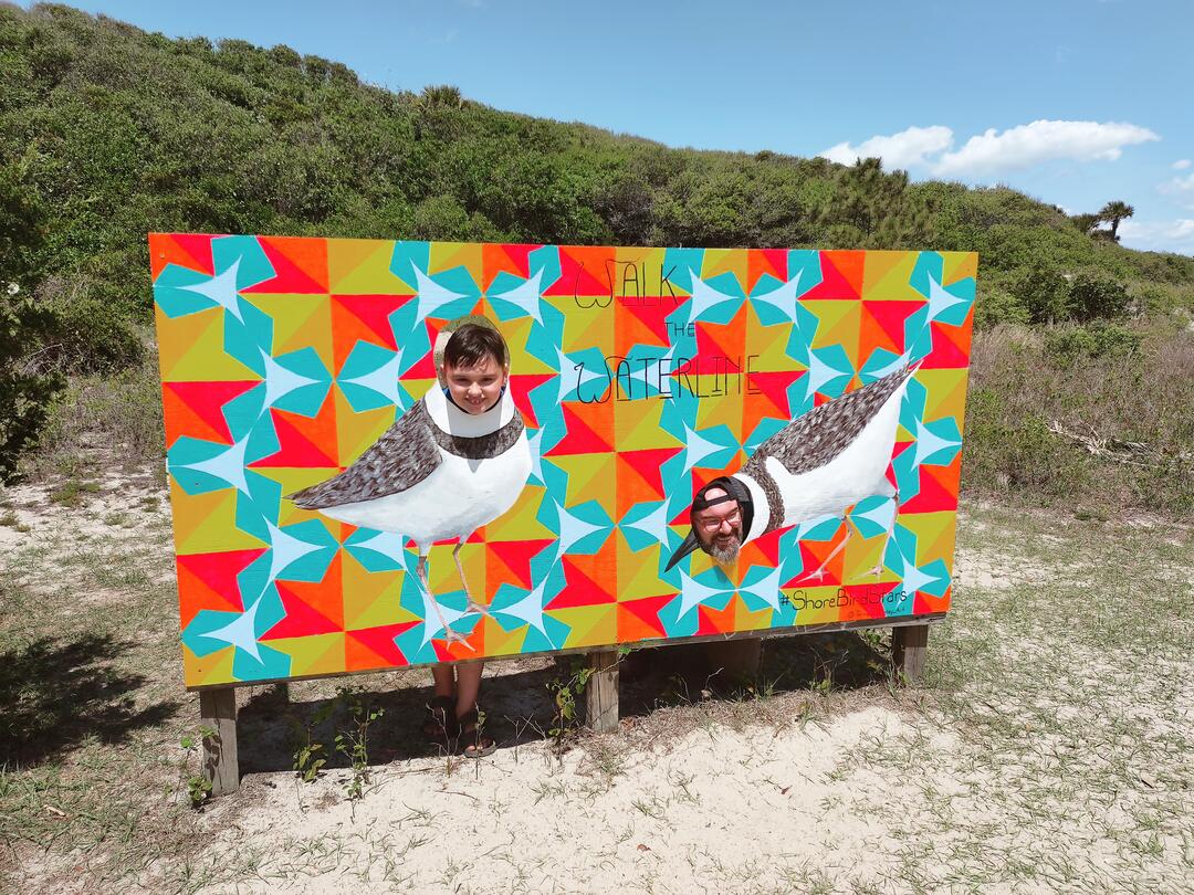 Two people pose in the photo cutout, with their faces on the bodies of Wilson's Plover shorebirds.